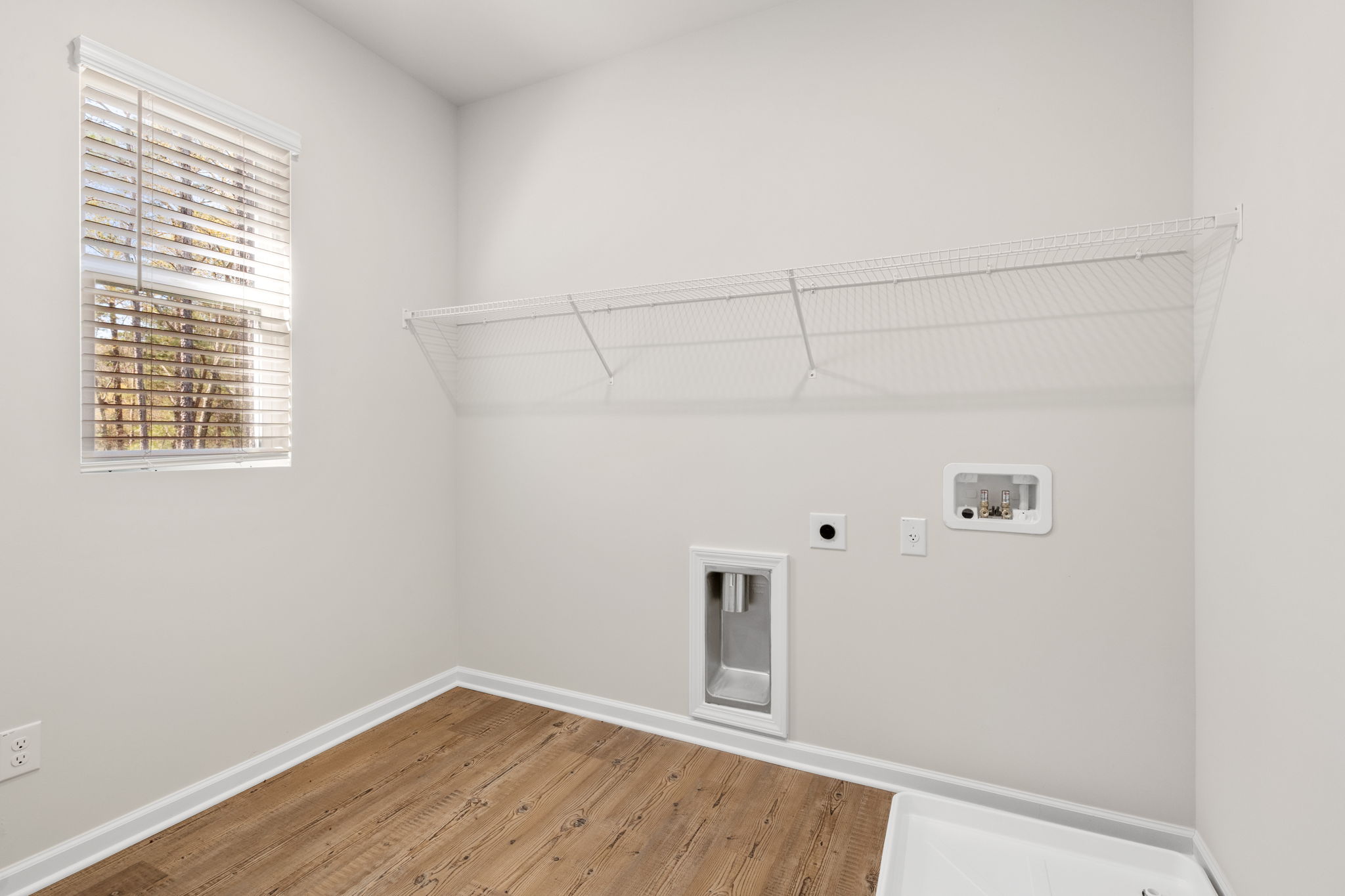 A room with a wood floor and a window with blinds.