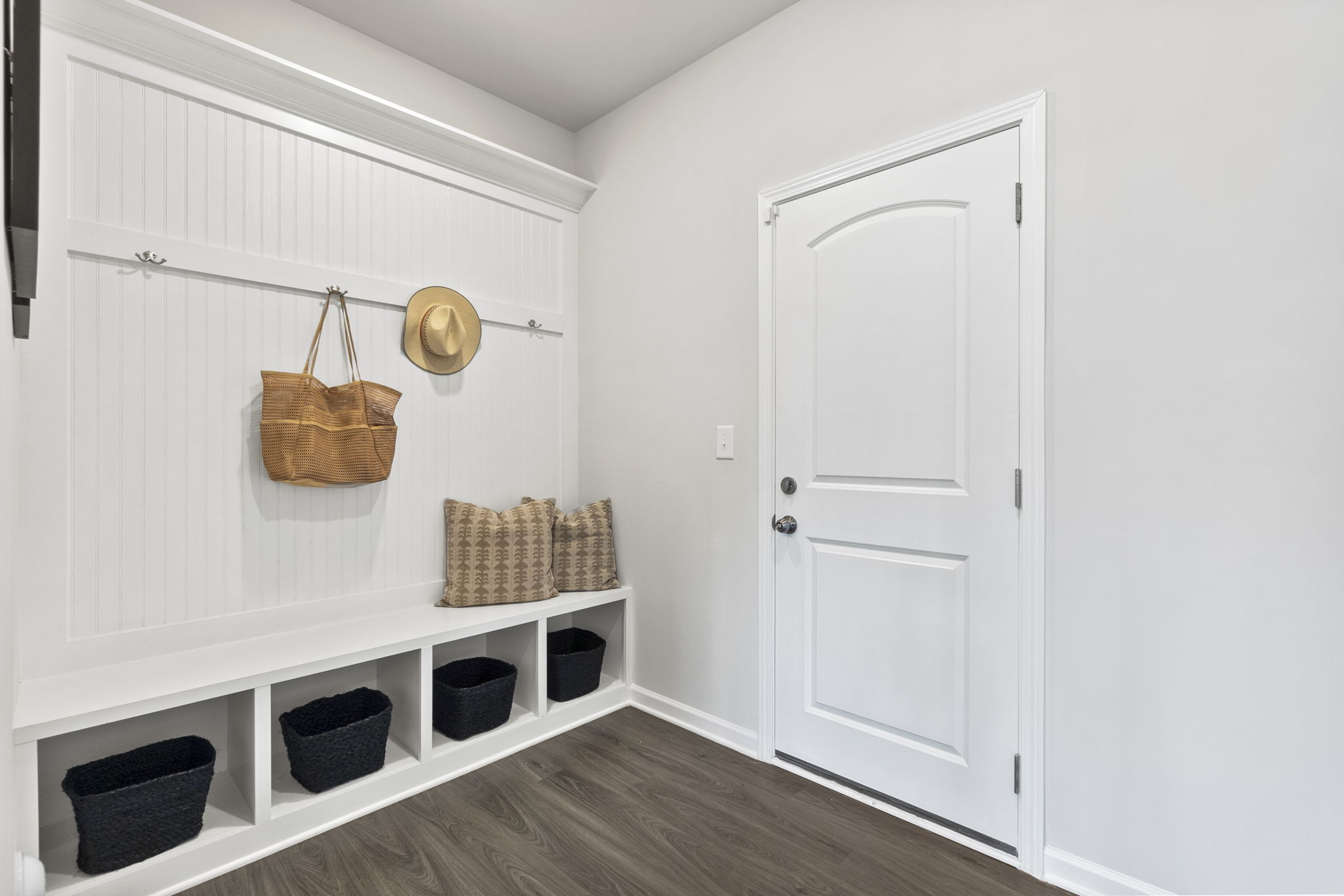 A white room with a white door and a white shelf with baskets.