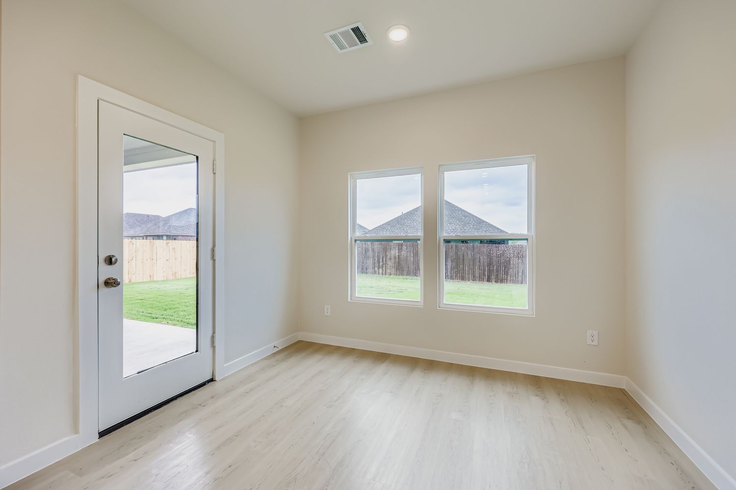 A room with a wood floor and a window with a view of a field and a house.