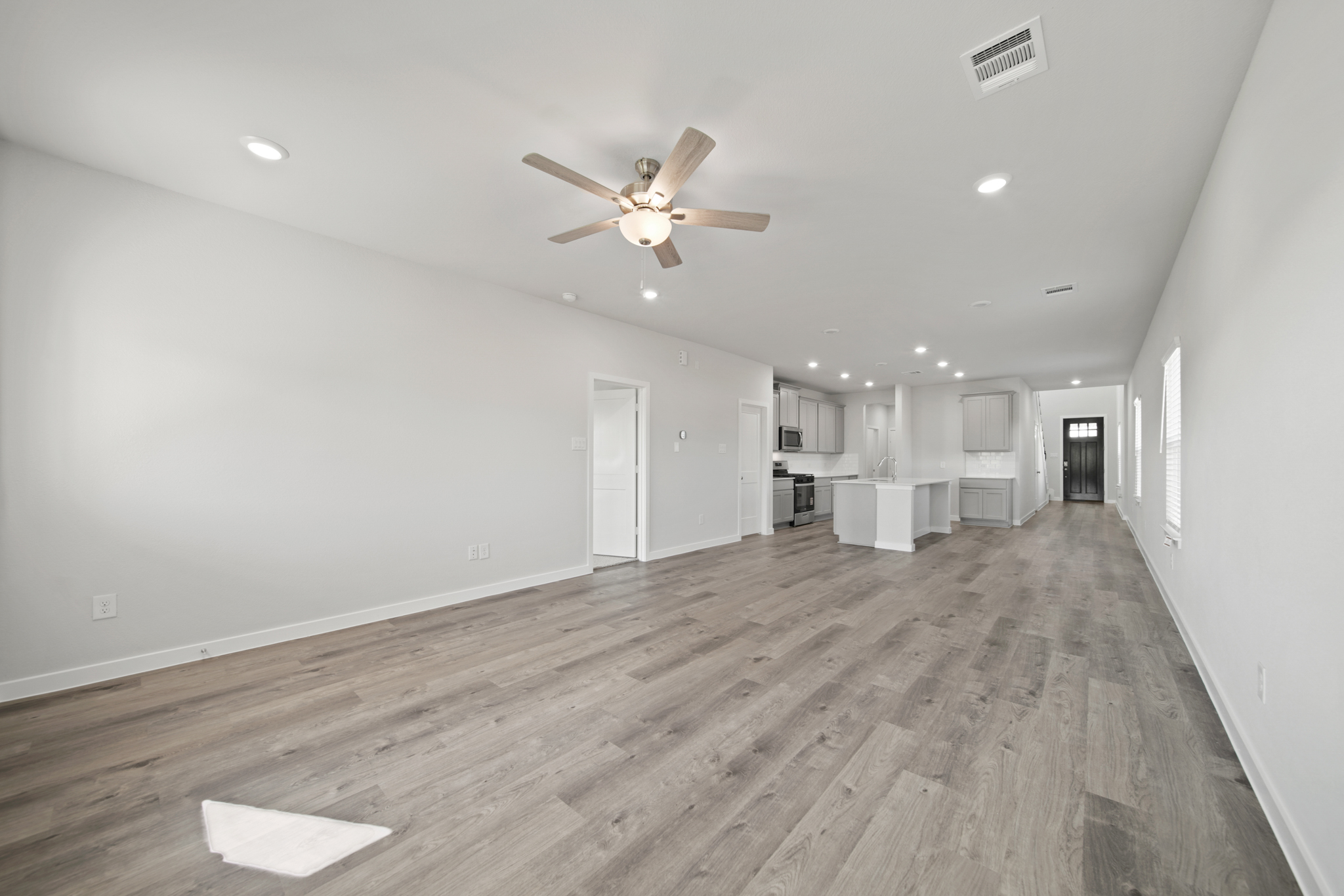A large empty room with a ceiling fan and a wood floor.