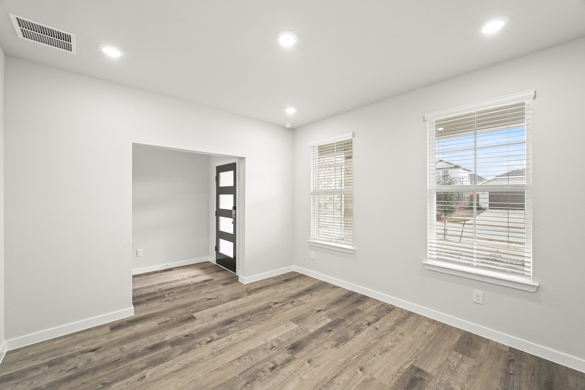 A room with a wood floor and a window with blinds.