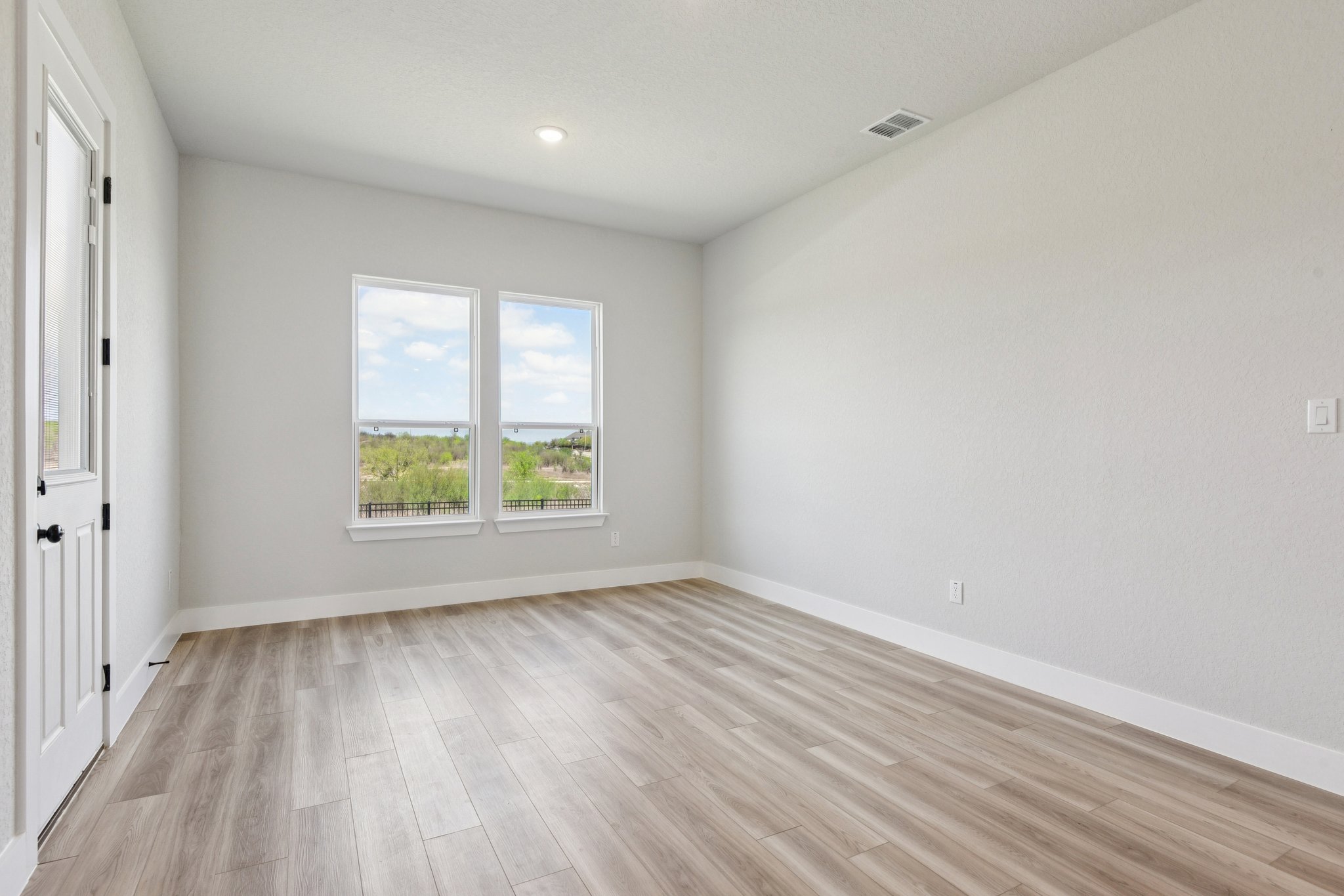 A room with a wood floor and a window with a view of trees.